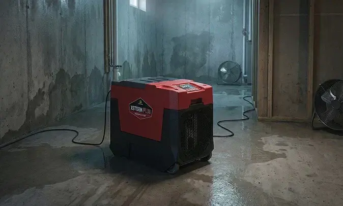 Dehumidifier running on a wet concrete basement floor in Fresh Meadows