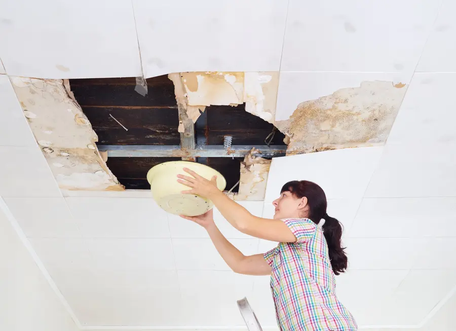 Resident catching water under an opened, leaking ceiling in a Fresh Meadows apartment
