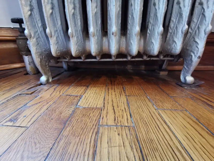 Cast iron radiator over a water-damaged oak floor in a Fresh Meadows home
